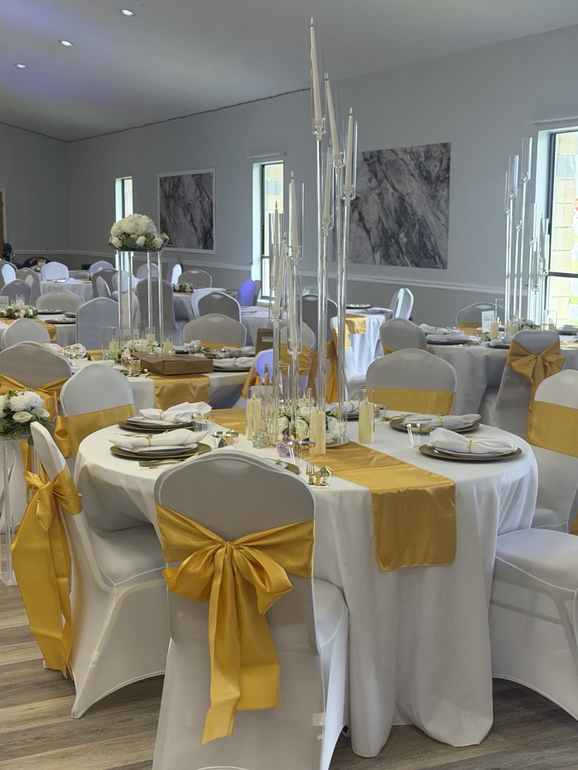 Round tables with white linens, gold chair bows, and tall candle centerpieces