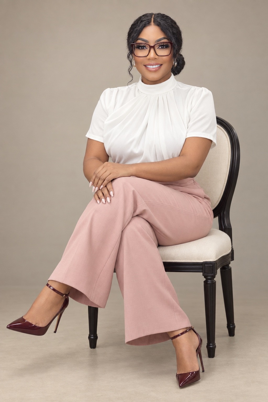 Tasha J. Neasman seated in a white blouse and rose trousers